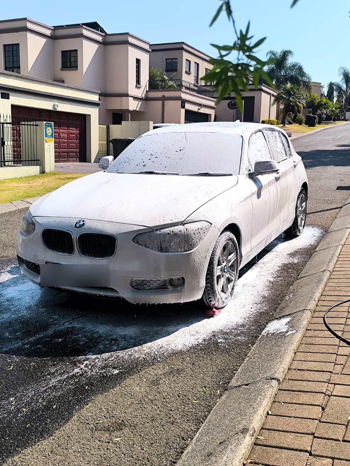 White BMW 1 Series under a full coat of snow foam on the kerb during a mobile wash