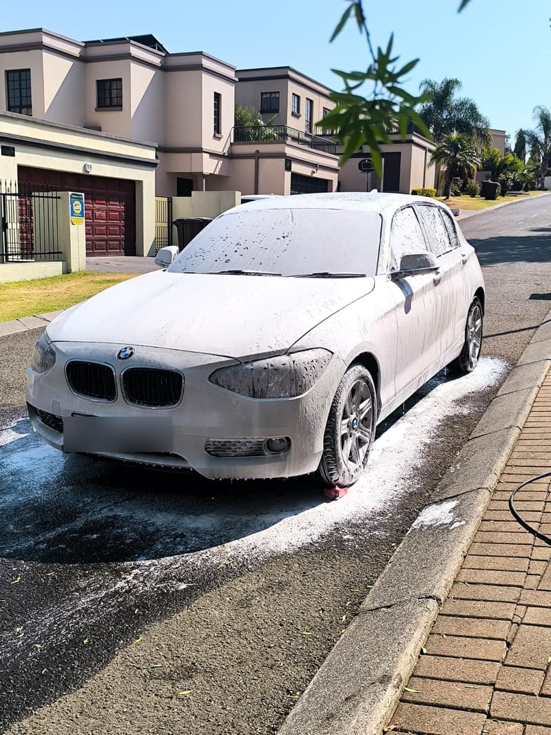 White BMW 1 Series under a full coat of snow foam on the kerb during a mobile wash