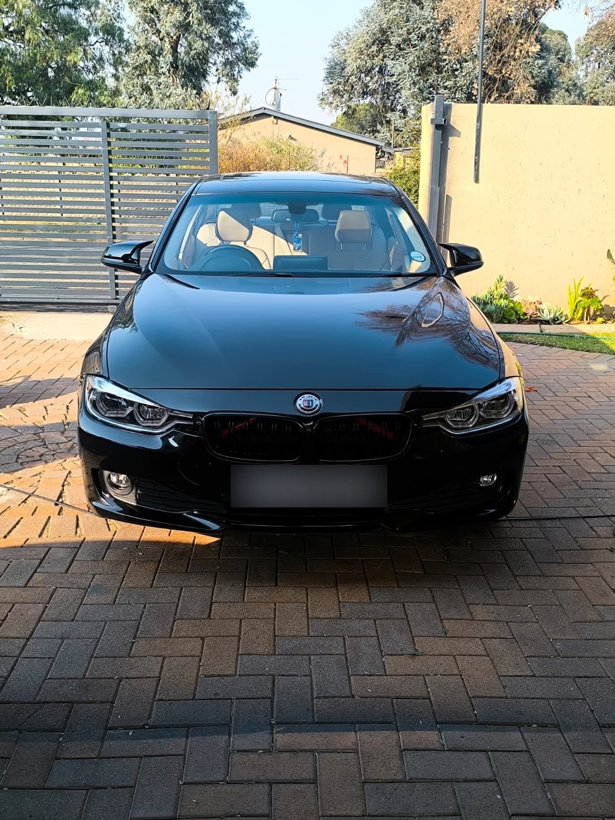Black BMW 3 Series finished on a brick driveway, front bumper and headlights cleaned
