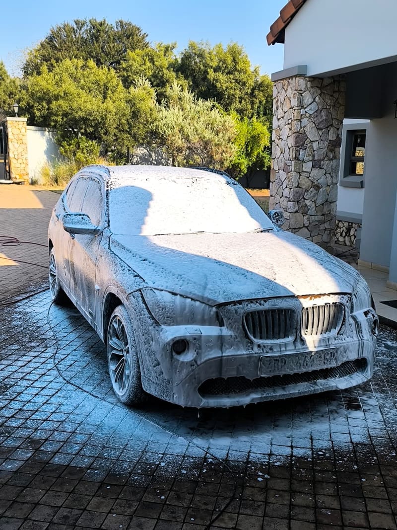 BMW SUV covered in snow foam on a driveway, foam lifting dirt before any contact wash