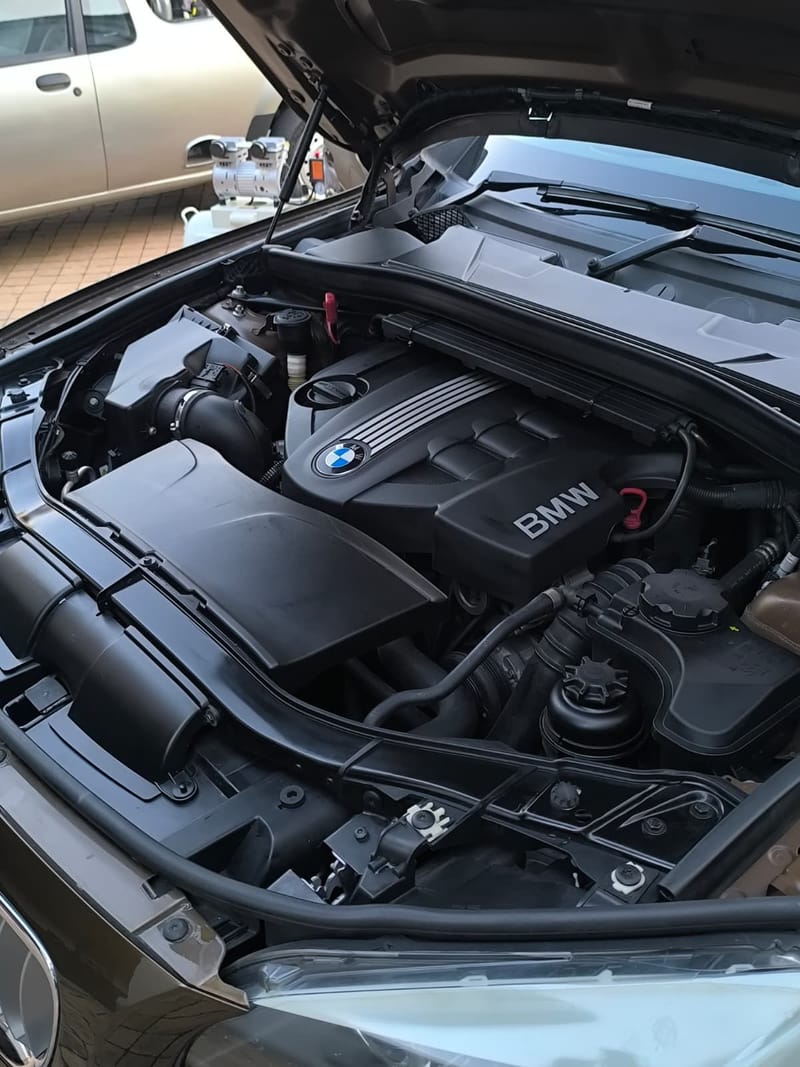 BMW engine bay after an engine bay clean and dress, with the mobile compressor set up alongside the car