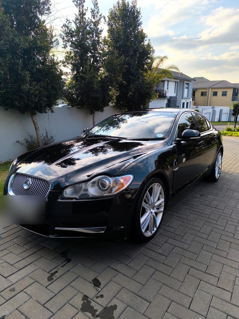Jaguar XF in gloss black after paint correction and a full detail, with clouds and trees mirrored in the bonnet