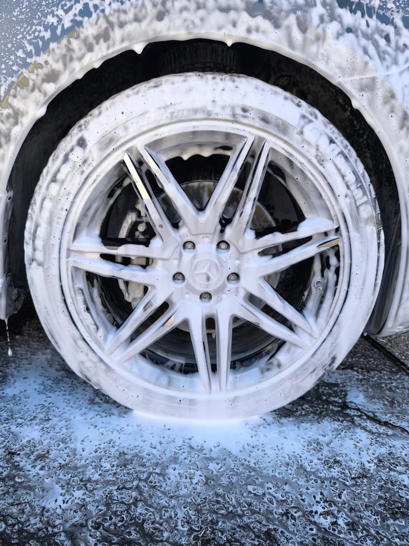 Close-up of an alloy wheel and tyre covered in snow foam during wheel and brake dust cleaning