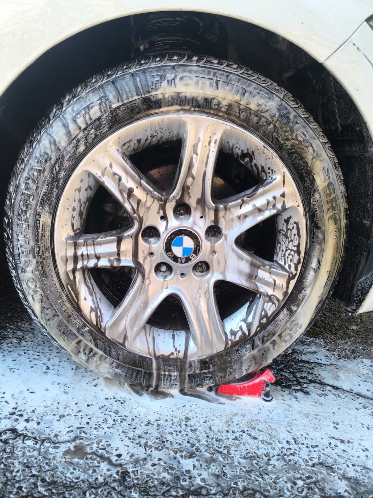 BMW alloy wheel under snow foam during the wheel and brake dust stage of a wash