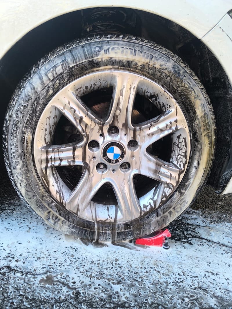 BMW alloy wheel under snow foam during the wheel and brake dust stage of a wash